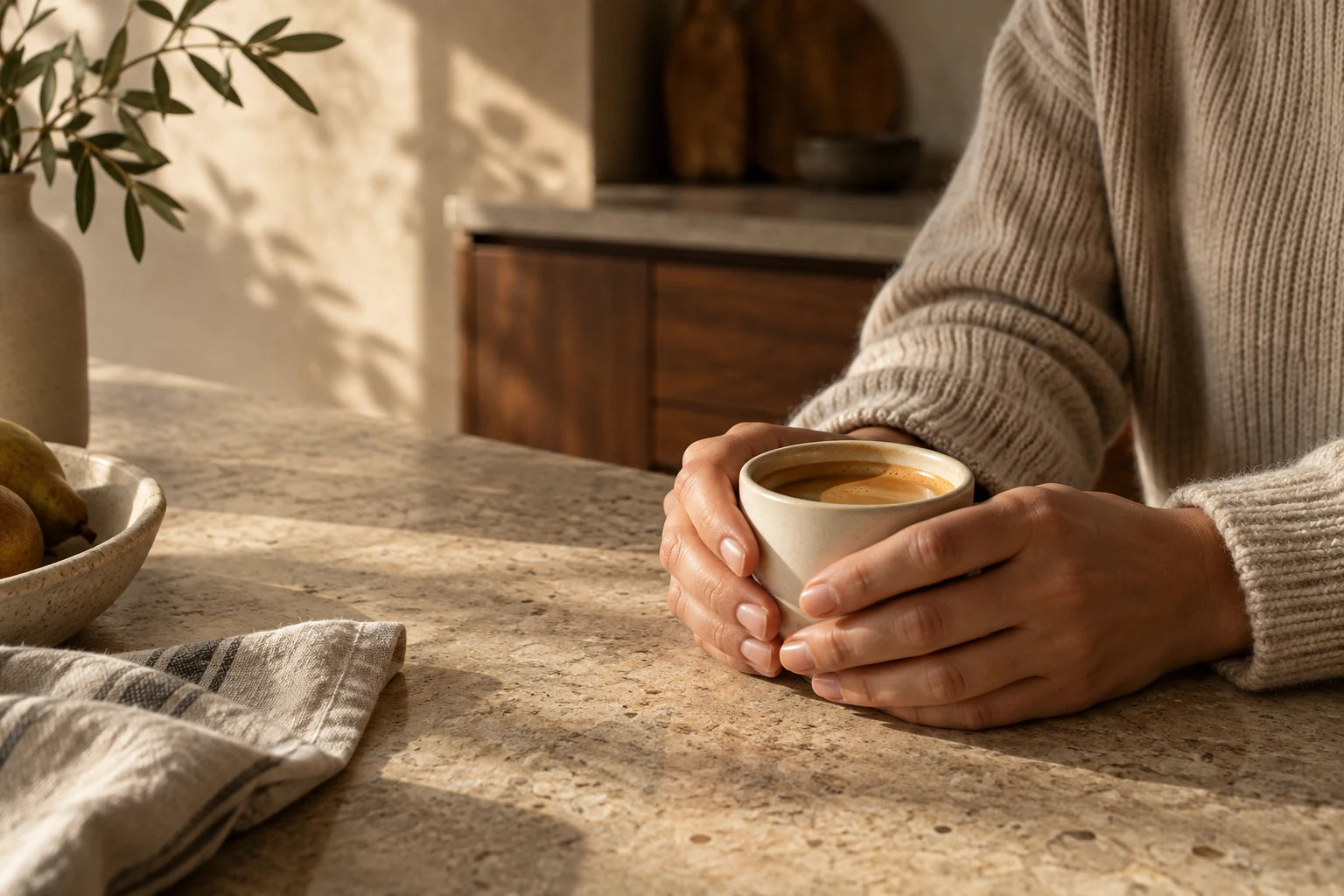 Hands wrapped around a warm cup of coffee at a sunlit kitchen counter